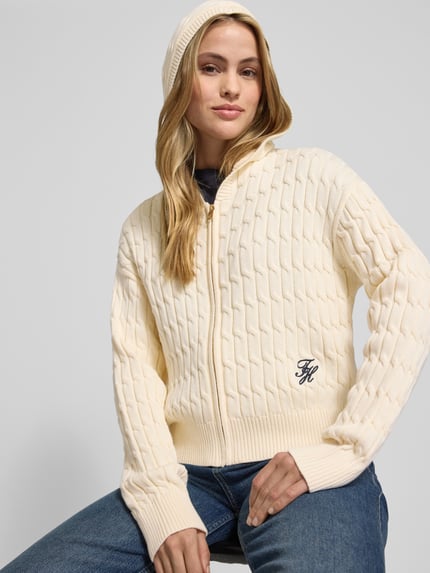 Vrouwenmodel draagt Comfort Fit Strickjacke aus reiner Baumwolle Modell 'CALICO' van Tommy Hilfiger in effen crème, kabelpatroon, met capuchon en rits, label-detail, ribboorden. Ganzkörperansicht van voren.