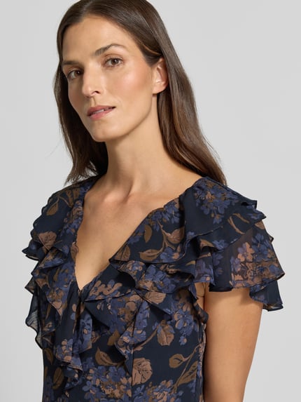 Frauenmodel trägt Eng anliegendes Abendkleid mit Rüschen von Lauren Ralph Lauren in Dunkelblau mit braunem Blumenmuster, Nahaufnahme Oberkörper. Damen Abendkleid von Lauren Ralph Lauren