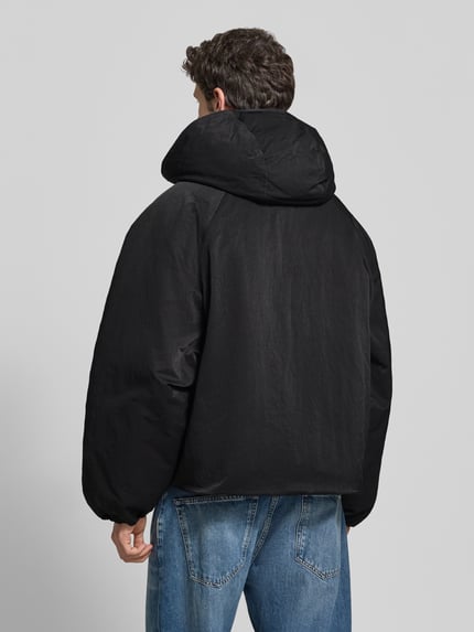 Männermodel trägt schwarze Relaxed Fit Bomberjacke mit Label-Patch Modell 'L’ATELIER' von RETERNITY, strukturierte Oberfläche, Ganzkörperansicht Rückansicht. Herren Bomberjacke mit Kapuze, Eingrifftaschen, Rückenlänge 70 cm, Schulterbreite 37 cm, Brustweite 80 cm, Ärmellänge 79 cm.