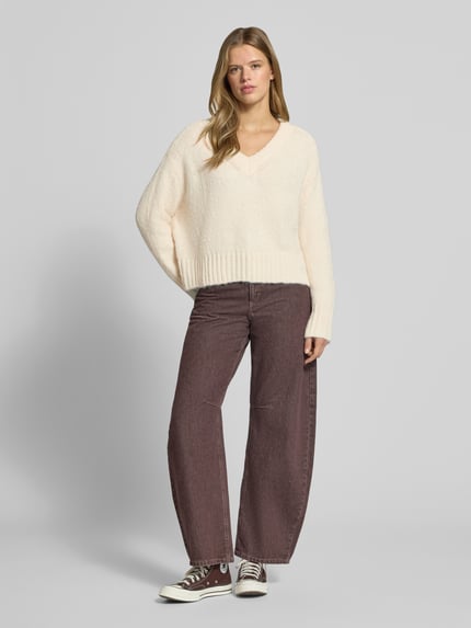 Frauenmodel trägt Pullover mit tiefem V-Ausschnitt von ONLY in Creme und weite braune Hose, Ganzkörperansicht von vorne. Damen Pullover von ONLY