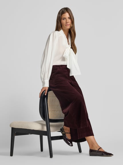 Frauenmodel trägt Weite Hose aus reiner Baumwolle Modell 'MELLI S' von Brax in Dunkelrot und weiße Bluse, Damen Weite Hose von Brax, Ganzkörperansicht von vorne.