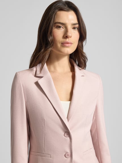 Vrouwenmodel draagt Slim Fit Blazer met reverskraag van More & More in lichtroze materiaalmix met viscose, knoopsluiting, paspelzakken, borstwijdte 46 cm, mouwlengte 64 cm, ruglengte 57 cm, nahaufnahme bovenlichaam.