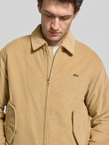 Männermodel trägt Bomberjacke mit Cordstruktur von LACOSTE, unifarben beige, Logo-Patch, Reißverschluss, Nahaufnahme Oberkörper.