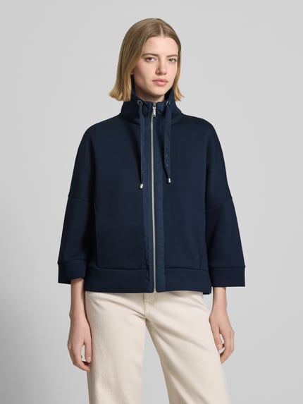 Frauenmodel trägt Regular Fit Sweatjacke mit Viskose-Anteil von Tom Tailor, dunkelblau, unifarben, Reißverschluss, Label Print, Stehkragen, 3/4-Arm, Scuba-Material, seitliche Eingrifftaschen, Ganzkörperansicht von vorne.