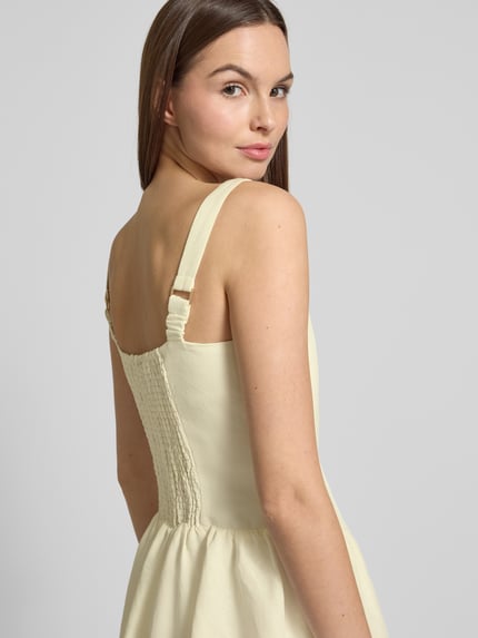 Frauenmodel trägt Cocktailkleid aus Leinen-Mix mit Smok-Details Modell 'Heidi' von Forever New, hellgelb, ausgestellter Schnitt, Minikleid, Rundhalsausschnitt, rückseitige Smok-Details, Leinen-Viskose-Mix, Nahaufnahme Rückenansicht.