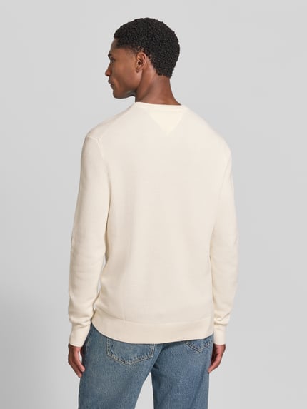 Männermodel trägt Regular Fit Pullover aus reiner Baumwolle von Tommy Hilfiger in Creme, kombiniert mit blauer Jeans, Ganzkörperansicht Rückansicht. Herren Pullover von Tommy Hilfiger