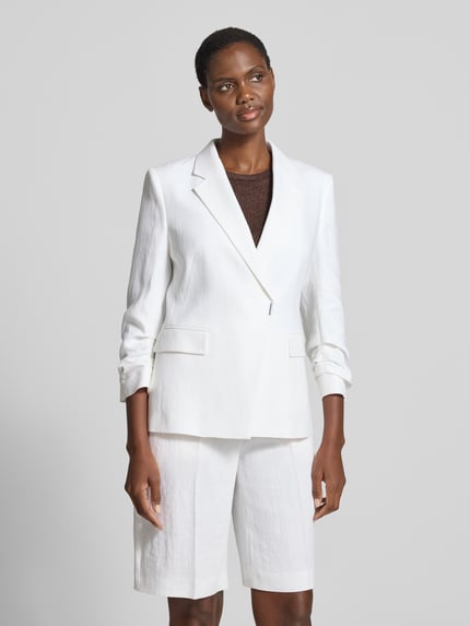 Frauenmodel trägt Slim Fit Kurzblazer aus Leinen-Viskose-Mix Modell 'JIA8' von BOSS in Melange-Optik, Twill, Reverskragen, 1-Knopf-Verschluss, Langarm, Pattentaschen, Materialverarbeitung: Leinen-Viskose-Mix, strahlendes Weiß, glatte Textur, Ganzkörperansicht von vorne.