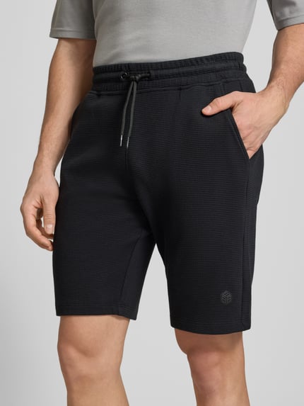 Männermodel trägt Straight Fit Shorts mit Logo-Stitching Modell 'Fillip' von Blend aus Reine Baumwolle mit Strukturmuster, Eingrifftaschen, Gesäßtaschen und elastischem Bund mit Tunnelzug, Nahaufnahme Oberkörper.