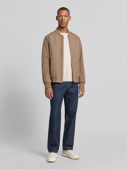 Männermodel trägt Regular Fit Jacke mit Stehkragen Modell 'Rapid' von CINQUE in Beige, Zweiwege-Reißverschluss, elastische Abschlüsse, Eingrifftaschen, Ganzkörperansicht von vorne. Rückenlänge 70 cm, Schulterbreite 49 cm, Brustweite 59 cm, Ärmellänge 69 cm.