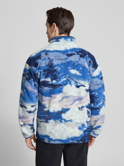 Männermodel trägt Regular Fit Pullover mit Logo-Patch von Columbia, fließ-Optik, stehend kołnierz, elastische wykończenia, ganzkörperansicht rückansicht, długość tyłu w rozmiarze M: 72 cm, długość rękawów w rozmiarze M: 49 cm.