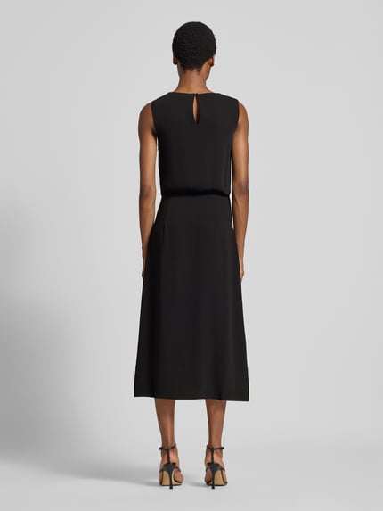 Frauenmodel trägt schwarzes, ärmelloses Midikleid mit Raffungen und taillierter Passform, Modell 'Zola' von GUIDO MARIA KRETSCHMER WOMAN, glatte Stoffstruktur, Schlüssellochausschnitt am Rücken, Ganzkörperansicht Rückansicht.