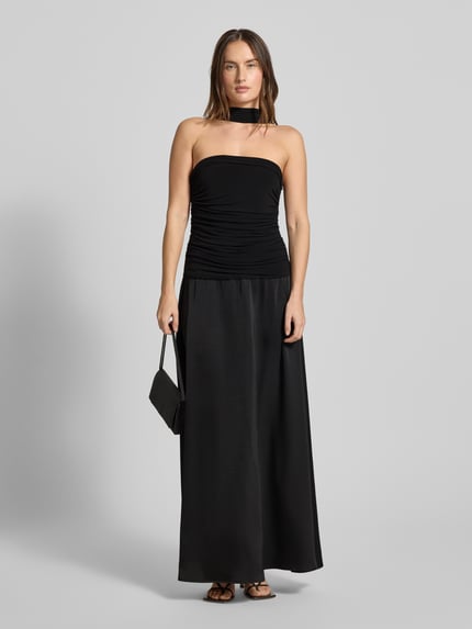Frauenmodel trägt Abendkleid mit Raffungen Modell 'Hamina' von Neo Noir, schwarzer Material-Mix mit Stretch-Anteil, A-Linie, Maxikleid, Ganzkörperansicht von vorne.