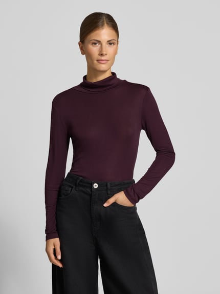 Frauenmodel trägt Slim Fit Longsleeve aus elastischem Baumwoll-Mix Modell 'OKTOBER' von COMMA in dunklem Violett, Rollkragen, glatte Struktur, Ganzkörperansicht von vorne.