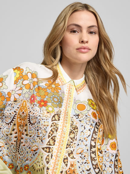 Modelka kobieca ma na sobie Boxy Fit Bluse aus Satin im Allover-Look od Herzensangelegenheit, wzór kwiatowy, kolor żółty i pomarańczowy, satynowa faktura, kołnierzyk koszulowy, zbliżenie na górną część ciała.
