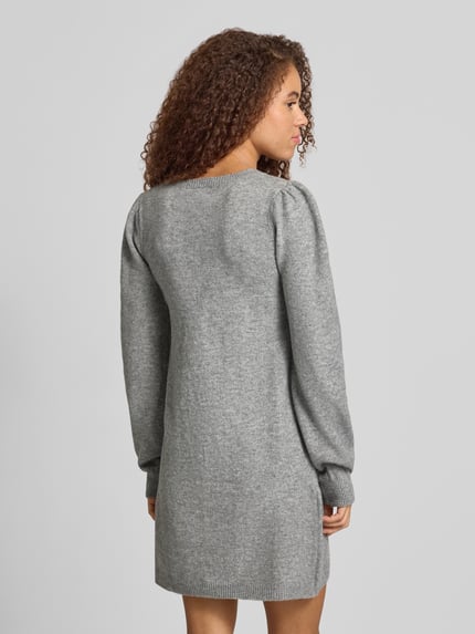 Frauenmodel trägt Strickkleid mit Puffärmeln von PIECES in grau melierter Strickoptik mit Rundhals, gerippten Abschlüssen, Ganzkörperansicht Rückansicht.