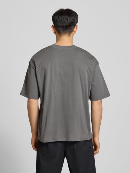 Männermodel trägt Oversized T-Shirt mit Logo und Rundhalsausschnitt van REVIEW in grijs, puur katoen, oversized fit, ruglengte maat M 68 cm, Ganzkörperansicht Rückansicht
