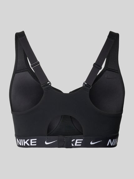 Mannelijk model draagt bustier met labeldetails en verstelbare bandjes van NIKE TRAINING, materiaalmix met stretch, nauwsluitende pasvorm, haakjessluiting, merkdetails, zwart, gladde en elastische textuur, detailopname rugaanzicht.