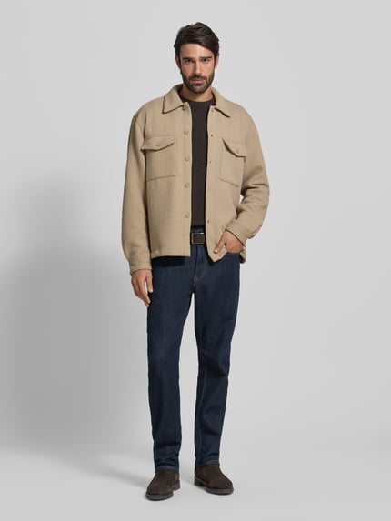 Męski model nosi Hemdjacke mit Knopfleiste od MCNEAL, mieszanka materiałów z dodatkiem wiskozy, luźny krój, kołnierzyk typu kent, kieszenie na piersi, kolor beżowy, gładka faktura, długość tyłu 69 cm przy rozmiarze M, widok całej sylwetki z przodu.