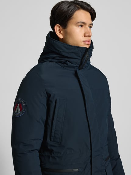 Männermodel trägt Parka mit Kapuze von Superdry in Dunkelblau, Material-Mix mit Stretch-Anteil und Label-Detail, Nahaufnahme Oberkörper.