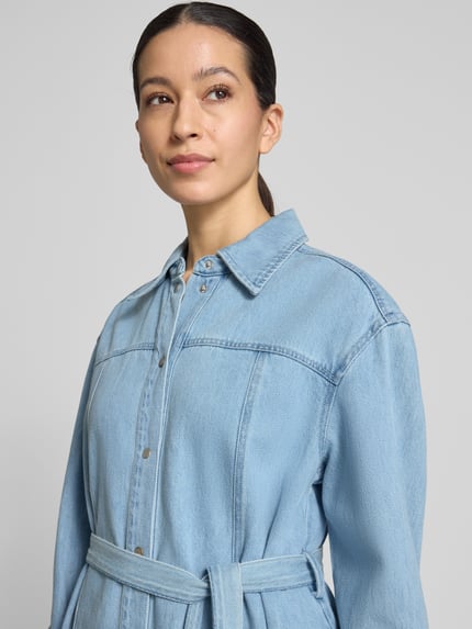 Frauenmodel trägt Knielanges Jeanskleid mit Bindegürtel Modell 'Kimmia' von mbyM, hellblauer Baumwoll-Mix, Hemdblusenkragen, Gerader-Schnitt, Nahaufnahme Oberkörper.