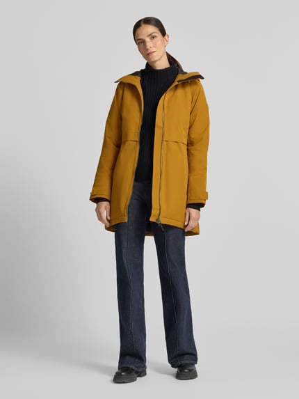 Frauenmodel trägt Regular Fit Parka mit Kapuze von Didriksons in Senfgelb, Zweiwege-Reißverschluss, Eingrifftaschen, Ganzkörperansicht von vorne. Rückenlänge, Schulterbreite, Brustweite und Ärmellänge in Größe 36 im Kontext.