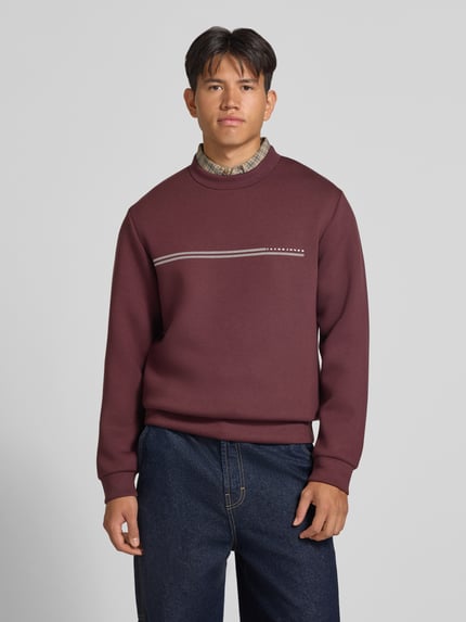 Männermodel trägt Relaxed Fit Sweatshirt mit Viskose-Anteil Modell 'Fusion' von JACK & JONES, bordeaux, Logo-Print, Ganzkörperansicht von vorne, Herren Sweatshirt, Material-Mix, lange Ärmel, elastische Abschlüsse, Rückenlänge und Ärmellänge je 66 cm, Struktur glatte Textur.