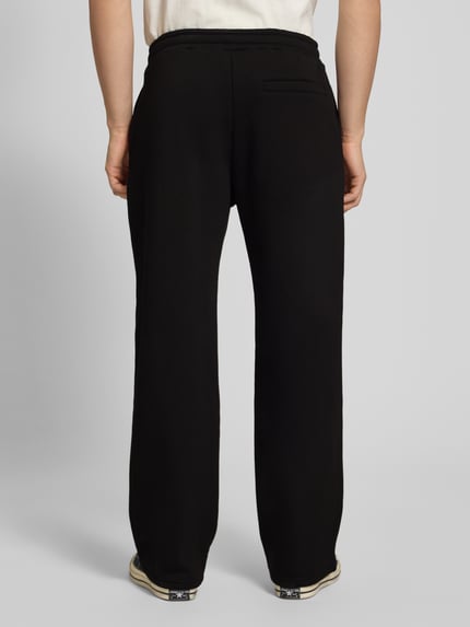 Männermodel trägt Sweatpants mit Logo-Print und Gesäßtasche von REVIEW, mieszanka bawełny, prosty krój, elastyczny pas, wpuszczane kieszenie, nadruk z logo, kieszeń z tyłu, długość wewnętrzna nogawki w rozmiarze M: 80 cm, widok całej sylwetki z tyłu