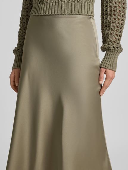 Vrouwenmodel draagt midirok uit satijn met ritssluiting van Juvia, dames midirok, smalle pasvorm, midilengte, detailopname taille.