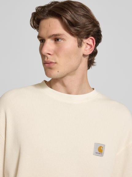 Männermodel trägt T-Shirt mit Strukturmuster Modell 'Nelson' von Carhartt Work In Progress in Creme, Reine Baumwolle, Label-Detail, Rundhalsausschnitt, Relaxed-Fit, Nahaufnahme Oberkörper.