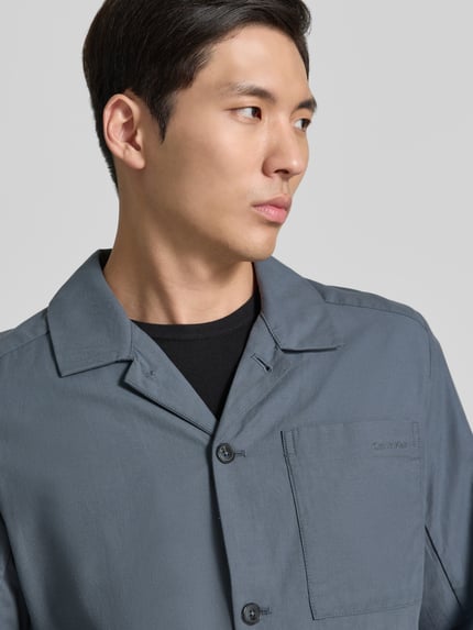 Männermodel trägt Oversized Hemdjacke aus Baumwoll-Lyocell-Mix von CK Calvin Klein, Optik: Unifarben, Label-Stitching-Applikation, Materialverarbeitung: Twill, Nahaufnahme Oberkörper.