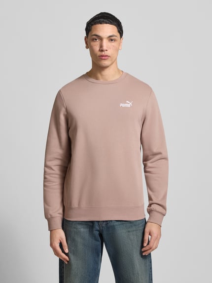 Męski model nosi Regular Fit Sweatshirt mit Logo-Stitching od PUMA PERFORMANCE, mieszanka bawełny, okrągły dekolt, elastyczne wykończenia, kolor jasnobrązowy, widok całej sylwetki z przodu.