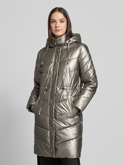 Frauenmodel trägt Steppmantel mit Kapuze Modell 'Jacket-Fa44ncy' von ZABAIONE in glänzender Metallic-Optik mit langen Ärmeln, seitlichen Eingrifftaschen, Kordel- und Metallakzenten, Reißverschluss sowie elastischem Taft, Ganzkörperansicht von vorne.