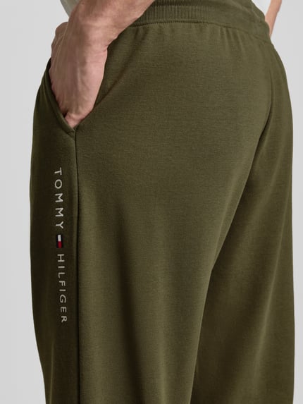 Mężczyzna nosi Comfort Fit Sweatpants aus Baumwoll-Mix von Tommy Hilfiger, kolor jednolity, aplikacja z logo, materiał bawełniany, detal bok, zbliżenie na biodro.