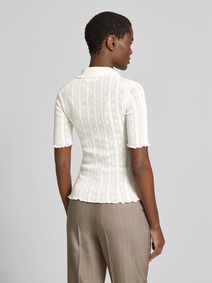Modelka kobieca nosi Slim Fit Poloshirt in Strick-Optik od Victoria Beckham, mieszanka bawełny, półprzezroczysty materiał, z krótkim rękawem, długość tyłu w rozmiarze S: 56 cm, jasny kolor, imitacja dzianiny, widoczna struktura, widok całej sylwetki z tyłu.