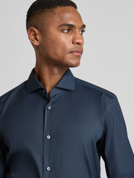 Männermodel trägt Slim Fit Business-Hemd mit Stretch-Anteil Modell 'Hank Hai' von BOSS, unifarben, Haifischkragen, Nahaufnahme Oberkörper.