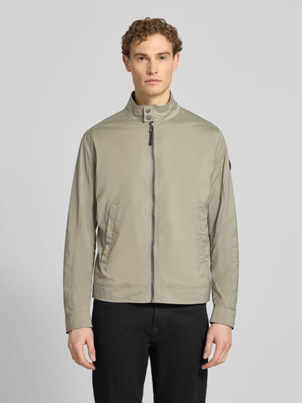 Männermodel trägt Jacke mit Stehkragen Modell 'Vicente' von JOOP! Collection in Beige, glatte Struktur, Reißverschluss, Eingrifftaschen, Ganzkörperansicht von vorne.
