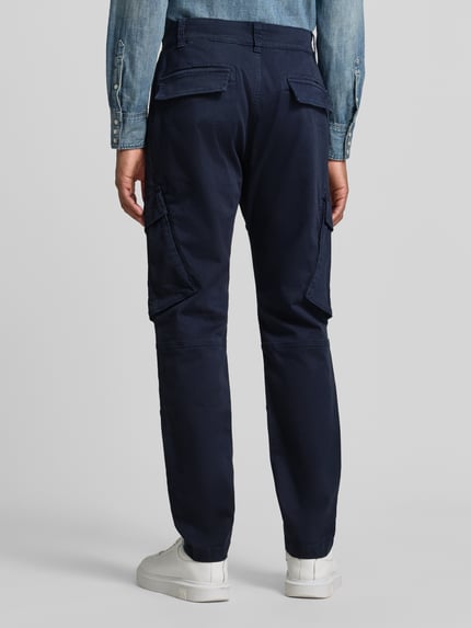 Männermodel trägt Straight Fit Cargohose aus mieszanka bawełny von MCNEAL, elastyczna mieszanka materiałów, wpuszczane kieszenie, kieszenie z tyłu, zapięcie na guzik i zamek błyskawiczny, Szerokość w rozmiarze M: 45 cm, Długość wewnętrzna nogawki w rozmiarze M: 80 cm, Ganzkörperansicht Rückansicht