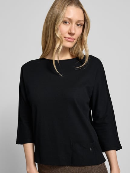 Frauenmodel trägt Shirt mit U-Boot-Ausschnitt und Label-Detail von Marc Cain, schwarz, straight Fit, Baumwoll-Mix, Nahaufnahme Oberkörper.