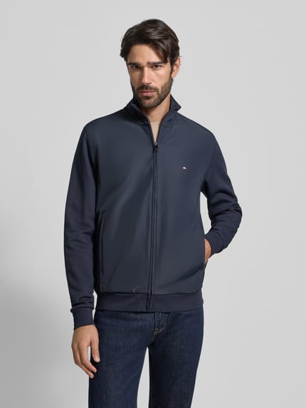 Männermodel trägt Regular Fit Blouson aus Baumwoll-Mix von Tommy Hilfiger in Dunkelblau, Zweiwege-Reißverschluss, unifarben, Ganzkörperansicht von vorne.