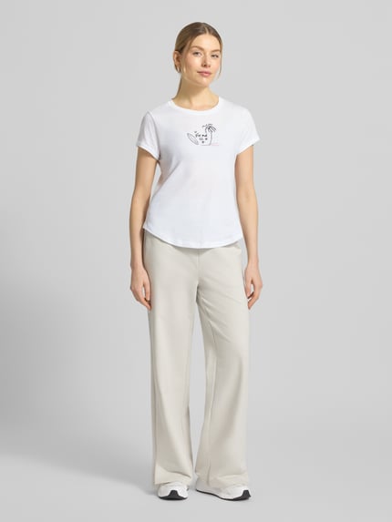 Modelka nosi T-Shirt mit Label-Print Modell 'DEBRA4' von FIRE + ICE, czysta bawełna, krój regular fit, okrągły dekolt, długość pleców w rozmiarze S: 58 cm, kolor biały z nadrukiem, widok całej sylwetki z przodu.