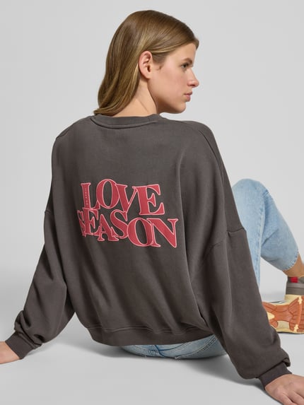 Frauenmodel trägt Oversized Sweatshirt mit Label-Stitching von OH APRIL in dunklem Grau, reine Baumwolle, Rundhalsausschnitt, Ganzkörperansicht Rückansicht.