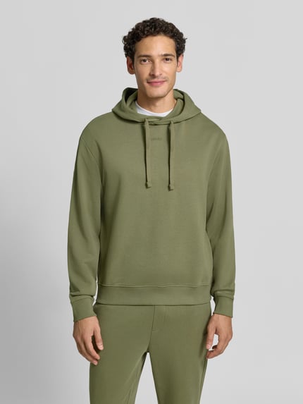 Männermodel trägt Relaxed Fit Hoodie aus reiner Baumwolle Modell 'Dapo' von HUGO in Olivgrün, glatte Struktur, Ganzkörperansicht von vorne. Herren Hoodie von HUGO.