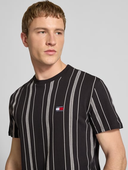 Männermodel trägt Regular Fit T-Shirt aus reiner Baumwolle van Tommy Jeans met allover patroon, label stitching, ronde hals, korte mouw, Nahaufnahme Oberkörper.