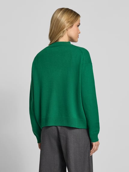 Vrouwenmodel draagt Oversized Pullover uit puur kasjmier van Anine Bing, groen, tricotlook met ribboorden, opstaande kraag, ruglengte maat S 55 cm, achteraanzicht van volledige lichaamslengte