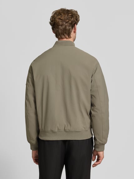 Mężczyznamodel nosi bomberkę z zamkiem błyskawicznym i wpuszczanymi kieszeniami 'Bomberjacke mit Reißverschluss und Eingrifftaschen' od JACK & JONES premium, krój regular fit, stójka, długość tyłu w rozmiarze M: 66 cm, szerokość ramion w rozmiarze M: 42 cm, szerokość klatki piersiowej w rozmiarze M: 60 cm, długość rękawów w rozmiarze M: 68 cm, kolor oliwkowy, tekstura gładka, widok całej sylwetki z tyłu.
