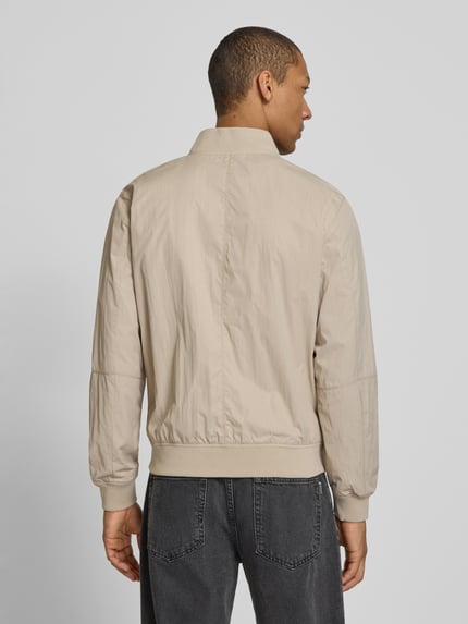 Männermodel trägt Regular Fit Bomberjacke mit Stehkragen von s.Oliver RED LABEL in Beige, unifarben, Rückansicht, Ganzkörperansicht Rückansicht.