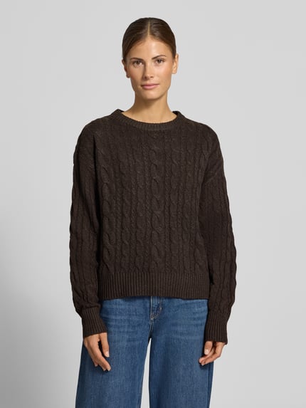 Frauenmodel trägt Pullover mit Zopfmuster Modell 'VMSEQUOIA' von VERO MODA in Dunkelbraun, Strick, unifarben, Rundhals, Rippsaum, Ganzkörperansicht von vorne.