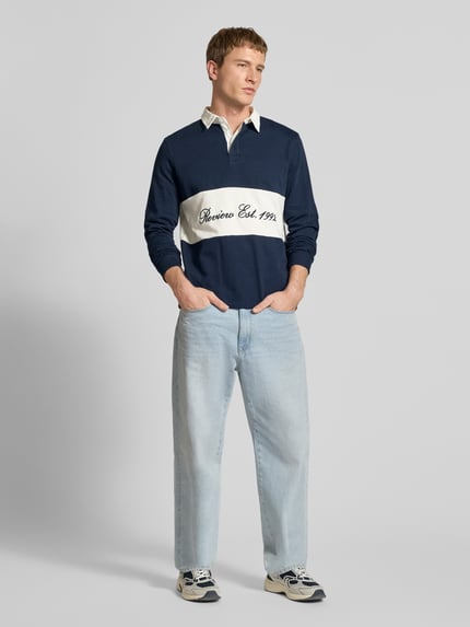 Mężczyzna nosi Regular Fit Langarm-Poloshirt mit Label-Stitching od REVIEW, bawełna, krój regular fit, wyhaftowane logo na pasku w kontrastowym kolorze, ukryta listwa guzikowa, długość tyłu w rozmiarze M: 68 cm, długość rękawów w rozmiarze M: 72 cm, widok całej sylwetki z przodu.