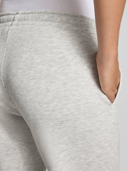 Frauenmodel trägt Wide Fit Sweatpants aus Baumwoll-Mix Modell 'Iconic' von Gina Tricot, hellgrau meliert, Nahaufnahme Hüfte, elastischer Bund mit Tunnelzug, Struktur fein, Damen Sweatpants von Gina Tricot, Baumwoll-Mix, Wide Fit, Modell 'Iconic', elastischer Bund mit Tunnelzug, Innenbeinlänge bei Größe S 80 cm