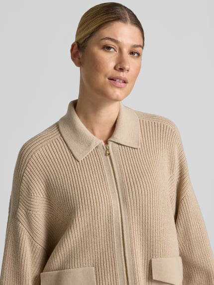 Frauenmodel trägt Strickjacke aus Schurwolle mit Pattentaschen von windsor. in Beige, sichtbare Strickstruktur, Nahaufnahme Oberkörper, Relaxed Fit